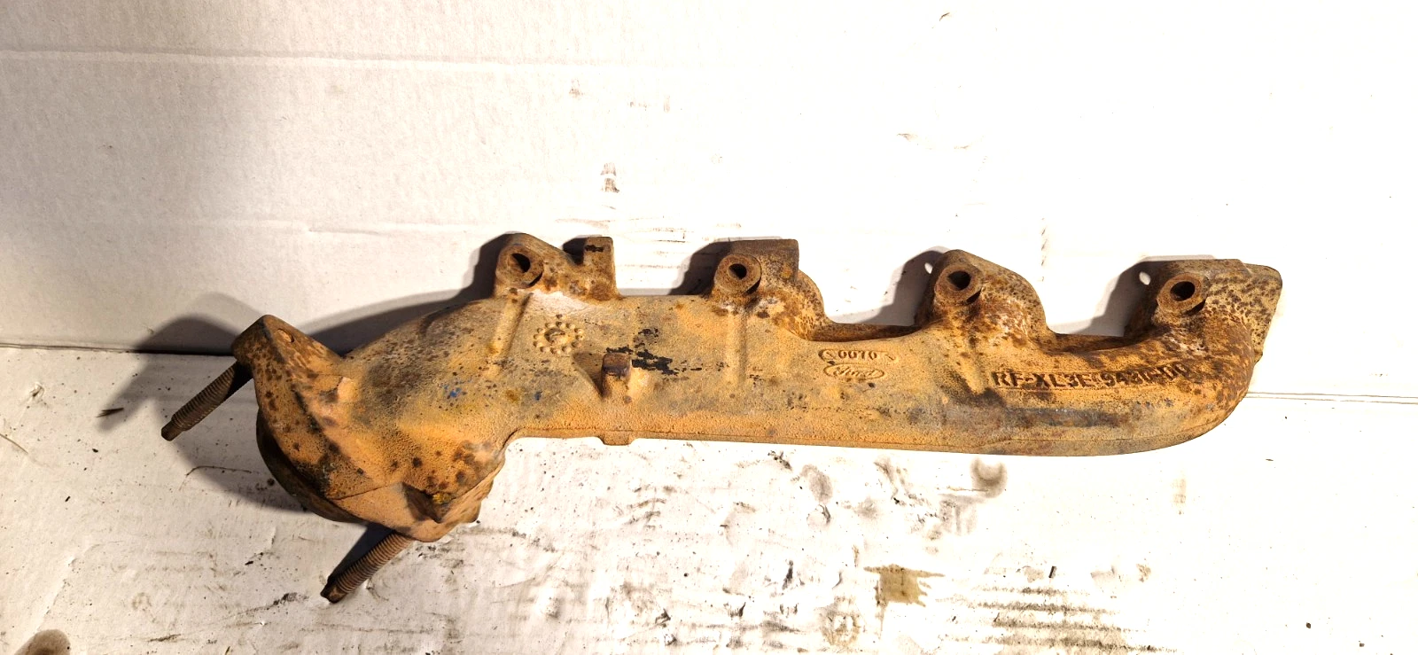 A rusty, old cast iron exhaust manifold for a 2003 Ford F150 showing signs of heavy wear and corrosion