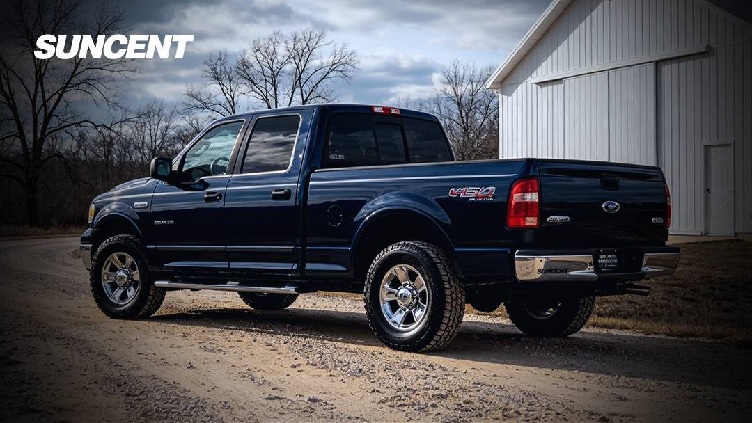 Navy blue 2003 Ford F-150 5.4 2V pickup driving on a gravel driveway with a white house in the background