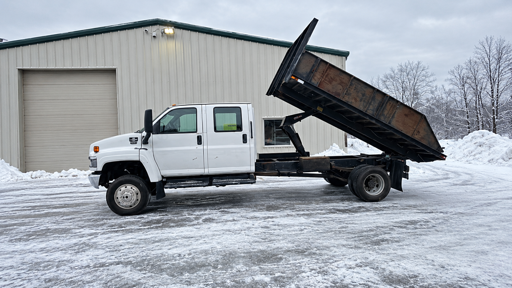 Chevy Kodiak C4500 dump truck with raised dump bed in a winter work yard